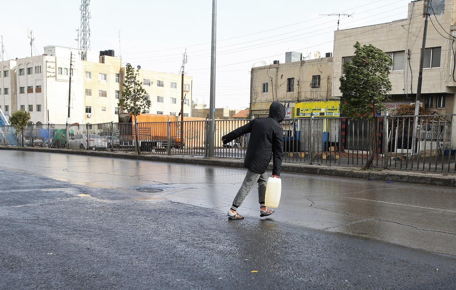 شخص يحمل "غالون" كاز تزامنا مع المنخفض الجوي في ماركا الشمالية في عمّان، 26/12/2019. (صلاح ملكاوي/ المملكة) 