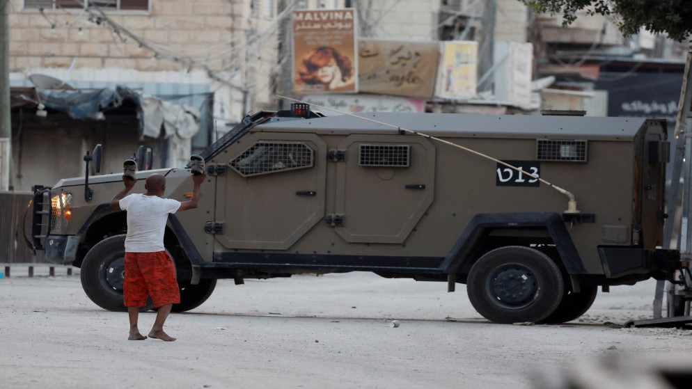 شاب فلسطيني حافي القدمين يرفع حذاءه أمام مركبة عسكرية إسرائيلية في الضفة الغربية المحتلة. (رويترز)