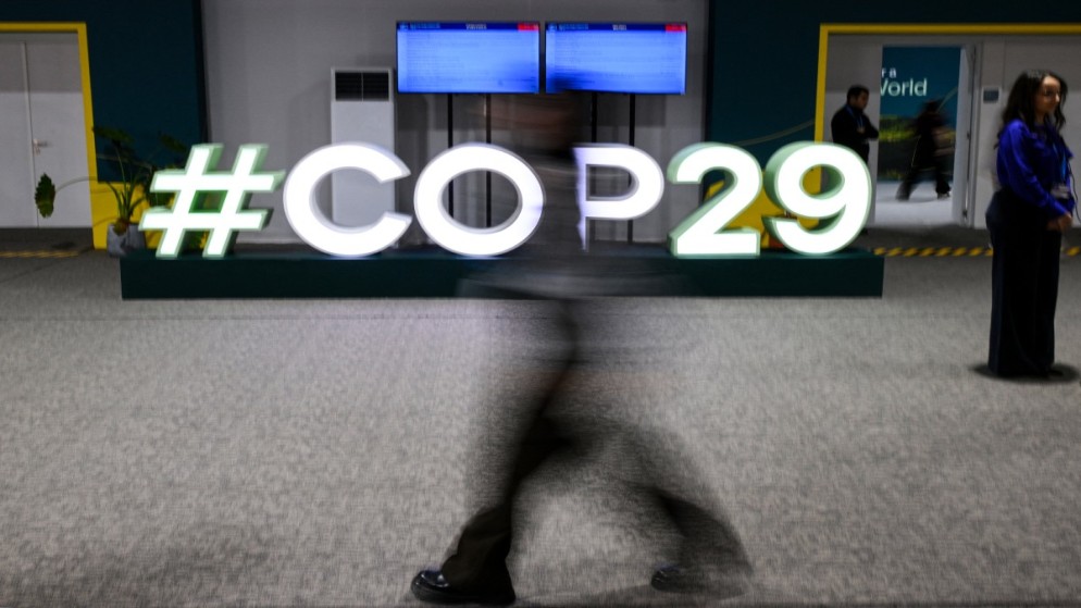 أشخاص يمرون أمام شعار COP29 خلال مؤتمر الأمم المتحدة لتغير المناخ (COP29) في باكو. أذربيجان. 21 نوفمبر 2024. (أ ف ب)