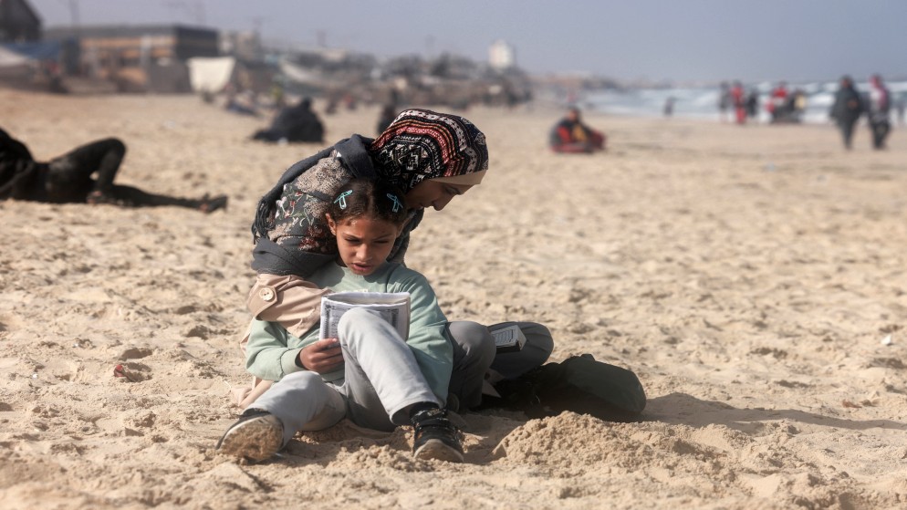 امرأة فلسطينية وفتاة تجلسان على الشاطئ المجاور لمخيم مؤقت للنازحين في رفح جنوب قطاع غزة .30 مارس 2024، (أ  ف ب)