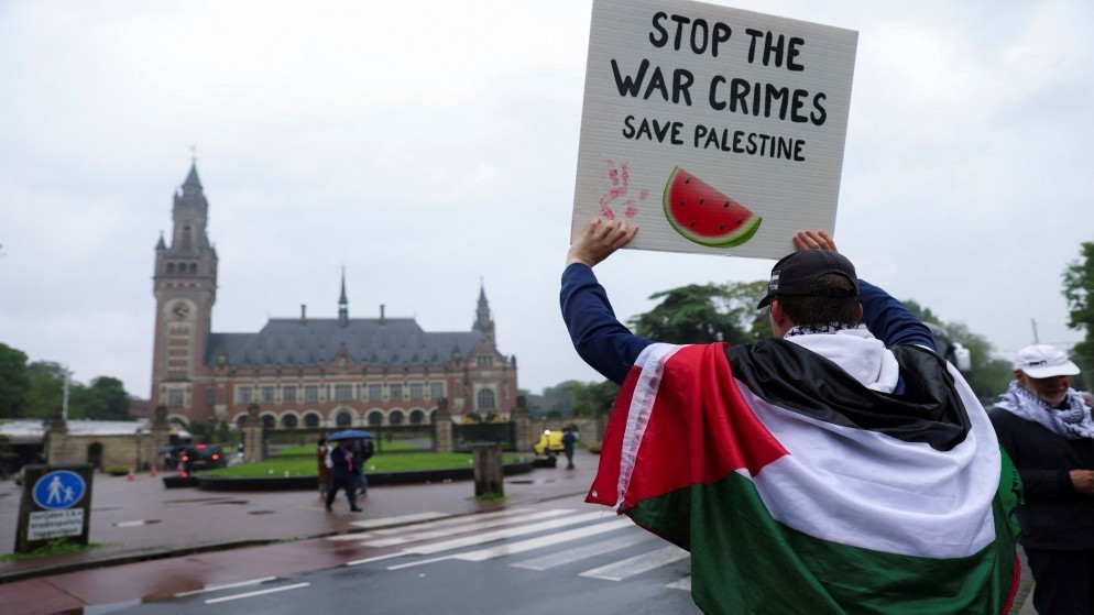 متظاهر يرفع لافتة أمام محكمة العدل الدولية تطالب بوقف جرائم الحرب في قطاع غزة. (رويترز)