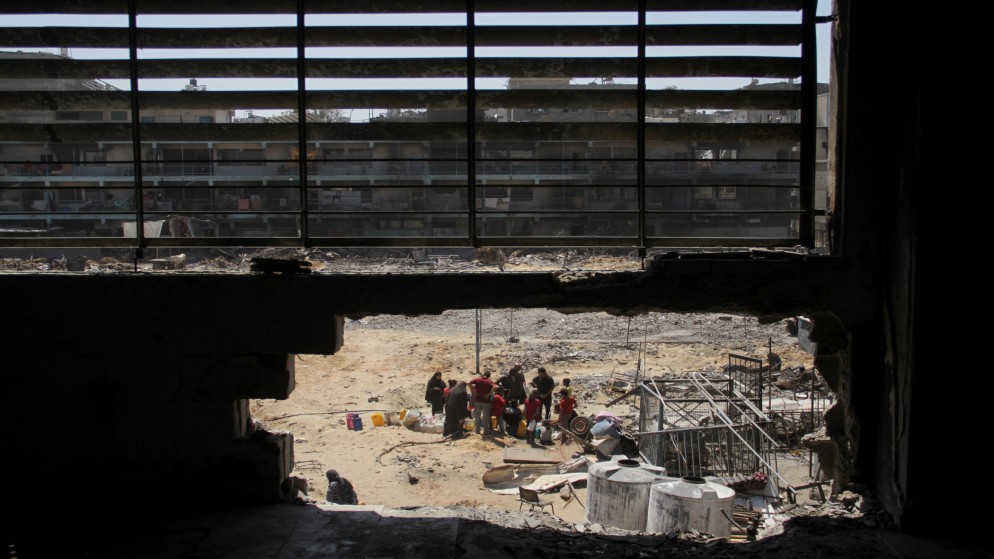 عائلة فلسطينية نازحة تجمع مياها في مدرسة مدمرة بفعل العدوان الإسرائيلي على قطاع غزة. (رويترز)