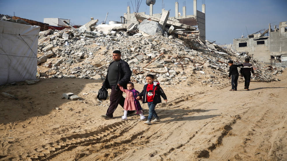 فلسطينيون يسيرون أمام أنقاض مبان دمرها العدوان الإسرائيلي في خان يونس جنوب قطاع غزة. 16 يناير، 2025. (رويترز)