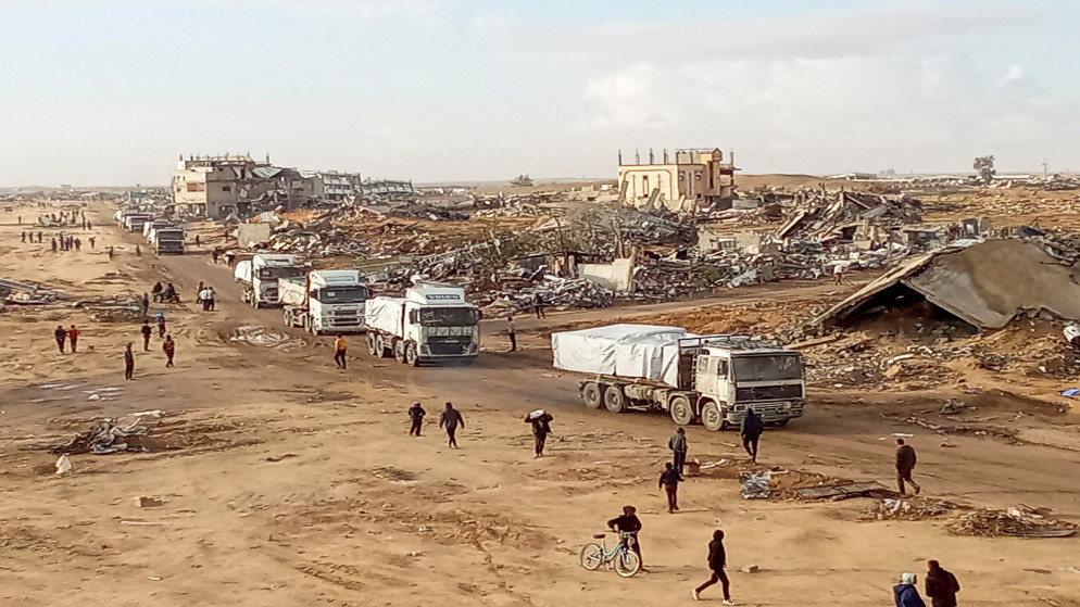 فلسطينيون يسيرون أمام شاحنات مساعدات، بعد وقف إطلاق النار بين إسرائيل وحماس، في رفح بجنوب قطاع غزة،  23 كانون الثاني 2025. (رويترز)