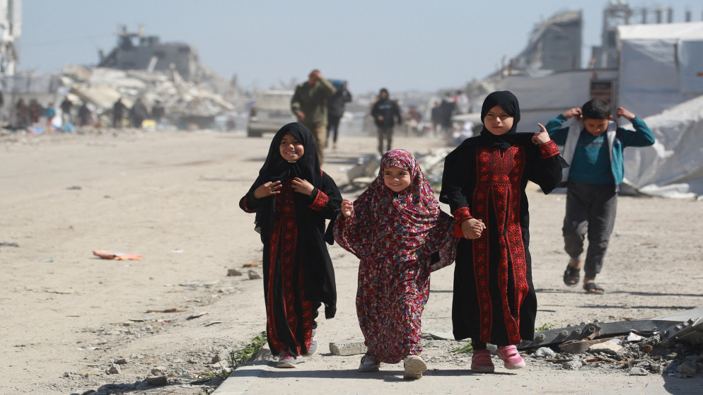 فتيات فلسطينيات يمررن بين أنقاض المباني وخيام النازحين في مخيم مؤقت غرب مدينة جباليا شمالي قطاع غزة، في 11 مارس/آذار 2025 (أ ف ب)