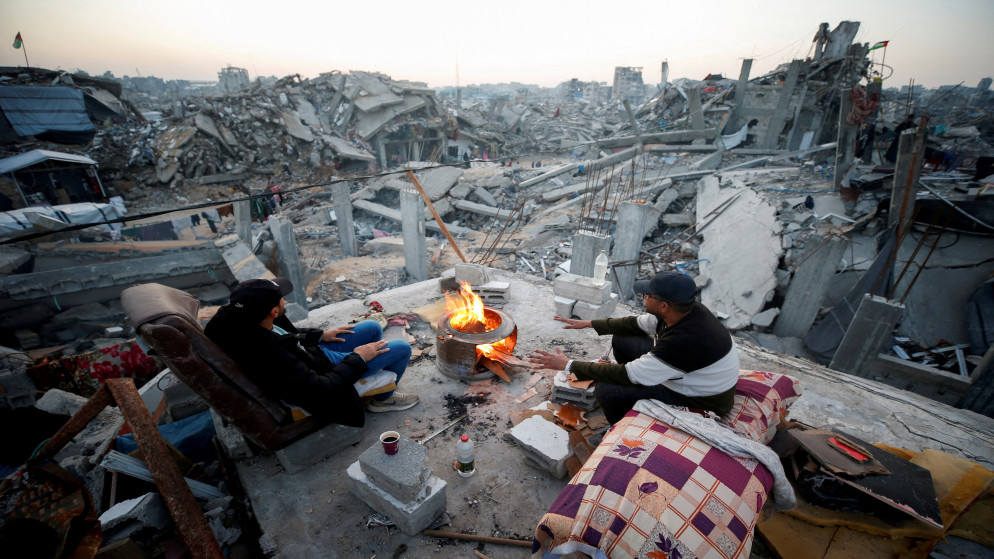 فلسطينيان يجلسان بجوار نار وسط أنقاض المباني المدمرة في مخيم جباليا شمال قطاع غزة، 17 شباط 2025. (رويترز)