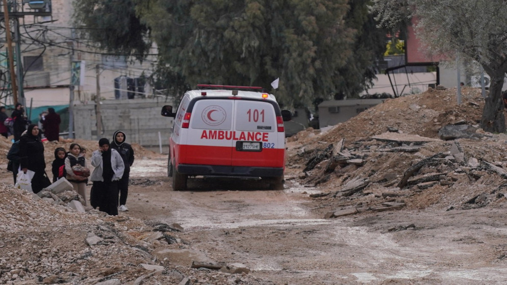 سيارة إسعاف فلسطينية تمر بجانب أشخاص يحملون أمتعتهم أثناء خروجهم من مخيم جنين للاجئين في الضفة الغربية المحتلة، 23 كانون الثاني 2025، (أ ف ب)